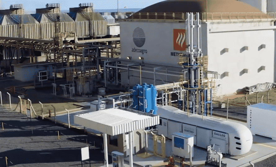 Vista aérea de un complejo industrial de la empresa Adecoagro destinado a la producción de bioenergía. En primer plano se observa una estación de compresión de biometano. Al fondo destaca un gran biodigestor de almacenamiento cilíndrico con techo abovedado junto a edificios operativos que muestran los logotipos corporativos de Adecoagro y Methanum.