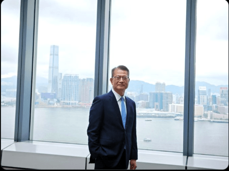 Fotografía en plano medio de Paul Chan Mo-po, secretario financiero de Hong Kong, sentado en un panel de debate corporativo. El funcionario viste traje oscuro formal.
