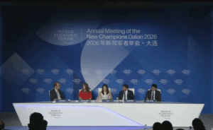Fotografía de un escenario iluminado durante una conferencia internacional del Foro Económico Mundial. Cuatro panelistas, vestidos con trajes ejecutivos formales, están sentados en sillones individuales manteniendo una discusión.