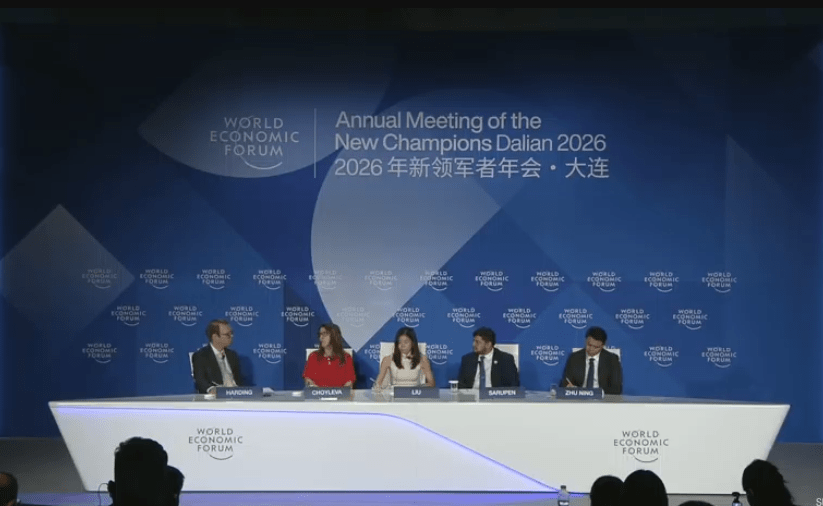 Fotografía de un escenario iluminado durante una conferencia internacional del Foro Económico Mundial. Cuatro panelistas, vestidos con trajes ejecutivos formales, están sentados en sillones individuales manteniendo una discusión.