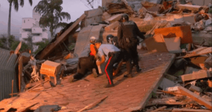 Fotografía del Terremoto en Venezuela. En la imagen se observa a cuatro rescatistas y funcionarios de seguridad pública, uno de ellos con la inscripción "POLICÍA CHACAO" en la espalda de su chaqueta negra, avanzando con precaución sobre una gran sección de techo derrumbada.