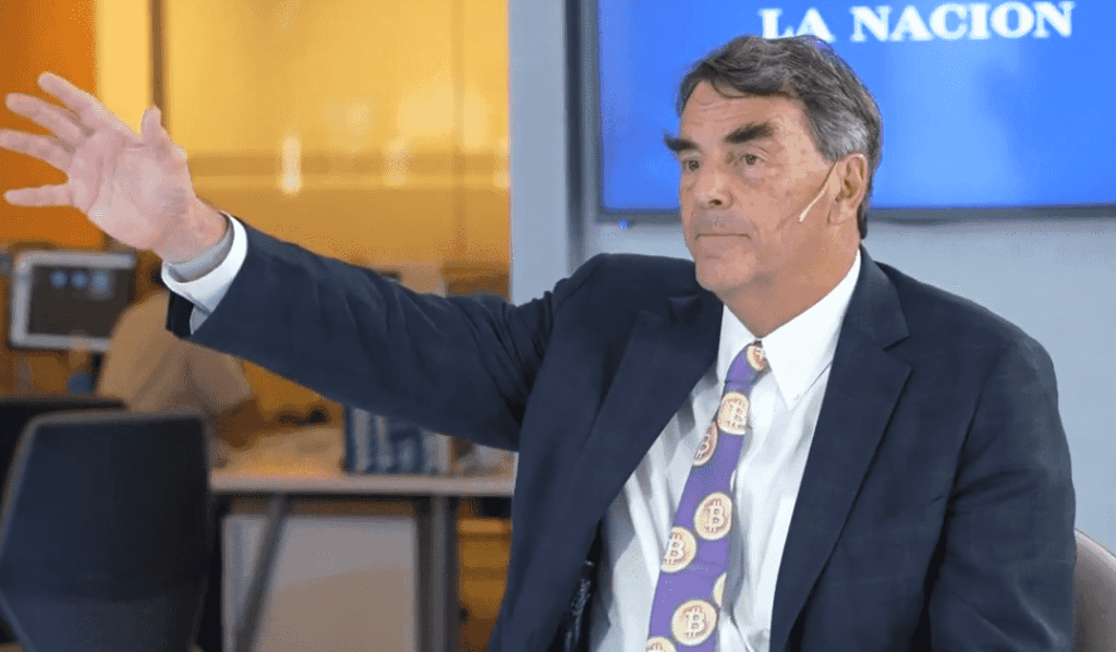 Tim Draper con traje oscuro y corbata estampada con el logode Bitcoin.