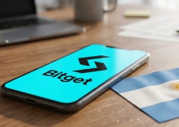 Teléfono mostrando el logo de Bitget en una mesa junto a la bandera de Argentina.