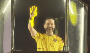Fotografía en plano medio de Abelardo de la Espriella hablando frente a un micrófono durante su discurso de victoria en Barranquilla. Viste camiseta de la sección de Colombia, gesticula con una mano en actitud firme y pantallas con iluminación del evento.