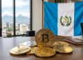 Bitcoin y criptomonedas junto a la bandera de Guatemala y una laptop sobre un escritorio.
