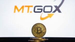Moneda física de bitcoin dorada sobre un escritorio con el logo de Mt.Gox de fondo.