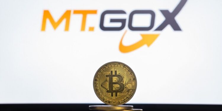 Moneda física de bitcoin dorada sobre un escritorio con el logo de Mt.Gox de fondo.