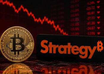 Moneda de bitcoin frente al logo de Strategy con gráficos bajistas en rojo.
