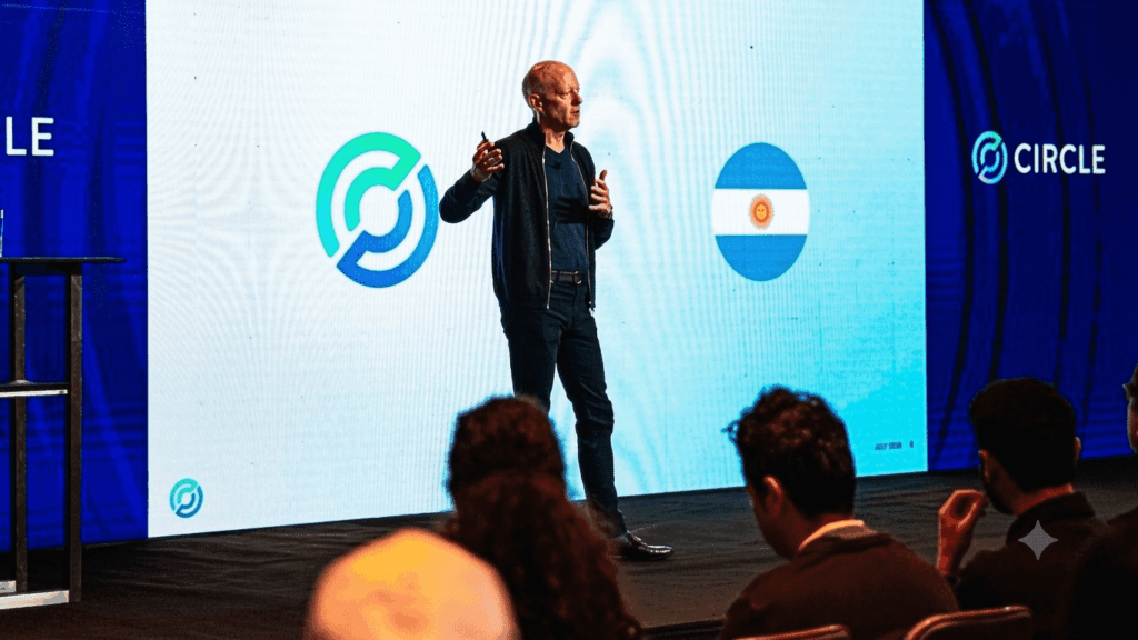 Una fotografía de Jeremy Allaire, CEO de Circle, de pie en un escenario y dando una presentación. Allaire, vestido con una chaqueta oscura y pantalones oscuros, sostiene un micrófono y gesticula con las manos mientras habla.