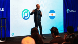 Una fotografía de Jeremy Allaire, CEO de Circle, de pie en un escenario y dando una presentación. Allaire, vestido con una chaqueta oscura y pantalones oscuros, sostiene un micrófono y gesticula con las manos mientras habla.