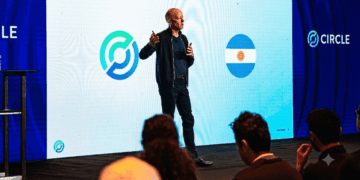 Una fotografía de Jeremy Allaire, CEO de Circle, de pie en un escenario y dando una presentación. Allaire, vestido con una chaqueta oscura y pantalones oscuros, sostiene un micrófono y gesticula con las manos mientras habla.