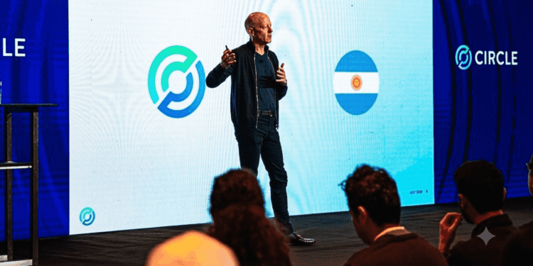 Una fotografía de Jeremy Allaire, CEO de Circle, de pie en un escenario y dando una presentación. Allaire, vestido con una chaqueta oscura y pantalones oscuros, sostiene un micrófono y gesticula con las manos mientras habla.