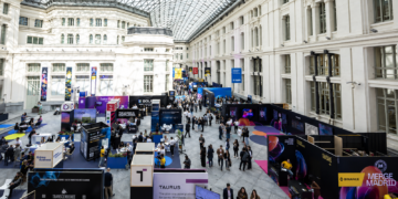 Feria tecnológica Merge Madrid 2025, con stands de criptomonedas y fintech en un gran recinto acristalado.