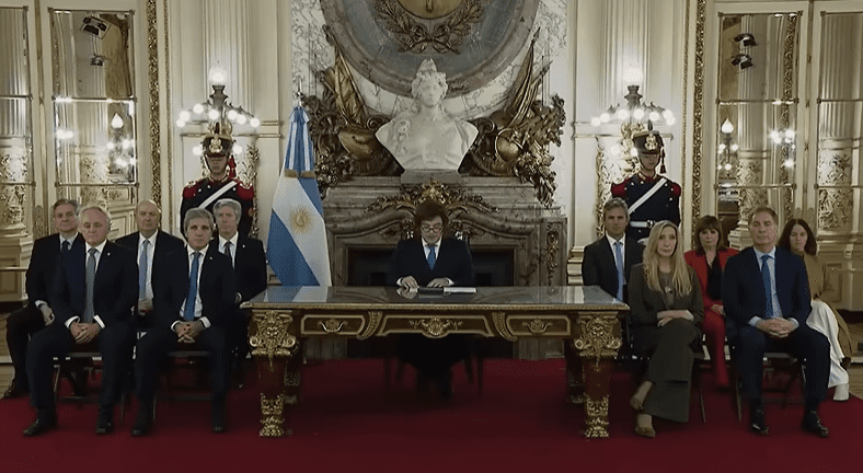 Fotografía del presidente argentino Javier Milei sentado al centro de una larga mesa de reuniones de madera, rodeado por los ministros y funcionarios de su gabinete en un salón de la Casa Rosada.