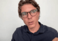 Primer plano de Oriol Blanch de Bitvavo, un hombre joven con gafas de carey y camisa polo azul oscuro, hablando y mirando hacia la izquierda del encuadre contra un fondo de pared blanca plana.