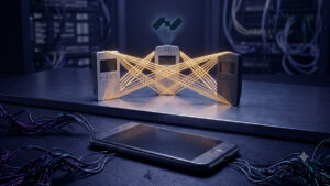 Composición digital conceptual sobre ciberseguridad. En primer plano, en un entorno oscuro, yace un teléfono inteligente con la pantalla agrietada rodeado de cables oscuros de aspecto siniestro, representando vulnerabilidad. Detrás, sobre una plataforma metálica elevada e iluminada, tres billeteras de hardware (hardware wallets) se mantienen de pie, interconectadas de forma segura mediante brillantes haces de luz dorada que simbolizan un esquema multifirma. Sobre el dispositivo central levita un holograma luminoso con el logotipo geométrico de Nunchuk. El contraste visual destaca la fragilidad del móvil frente a la fortaleza de la custodia en hardware.