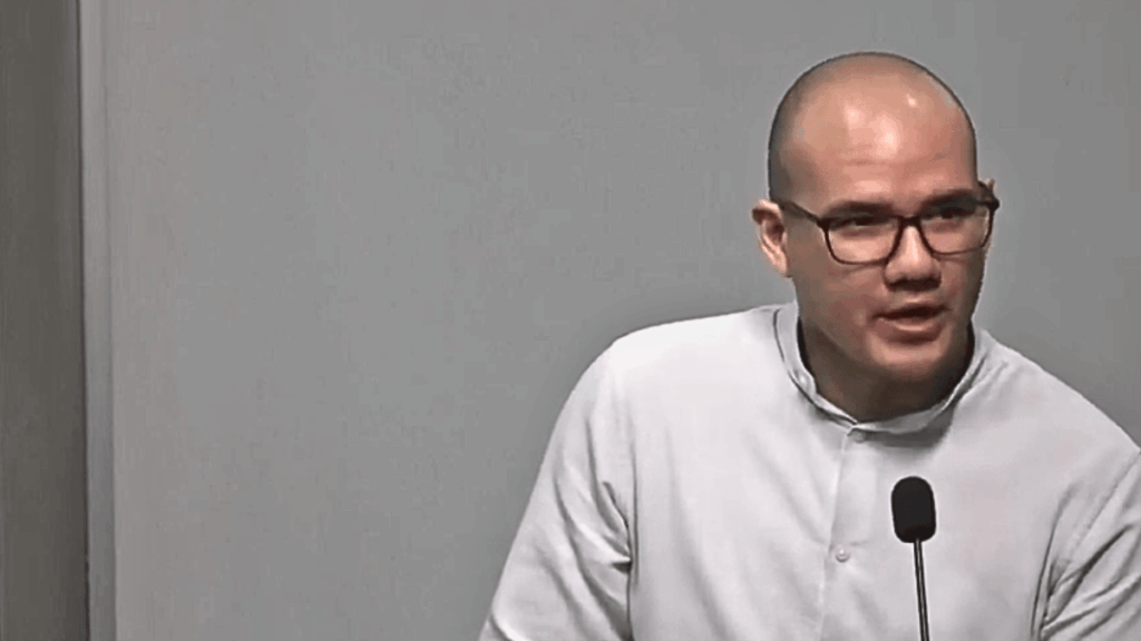 Rodrigo Icaza, hombre calvo con lentes de marco negro, viste camisa blanca y habla ante un micrófono durante una conferencia.