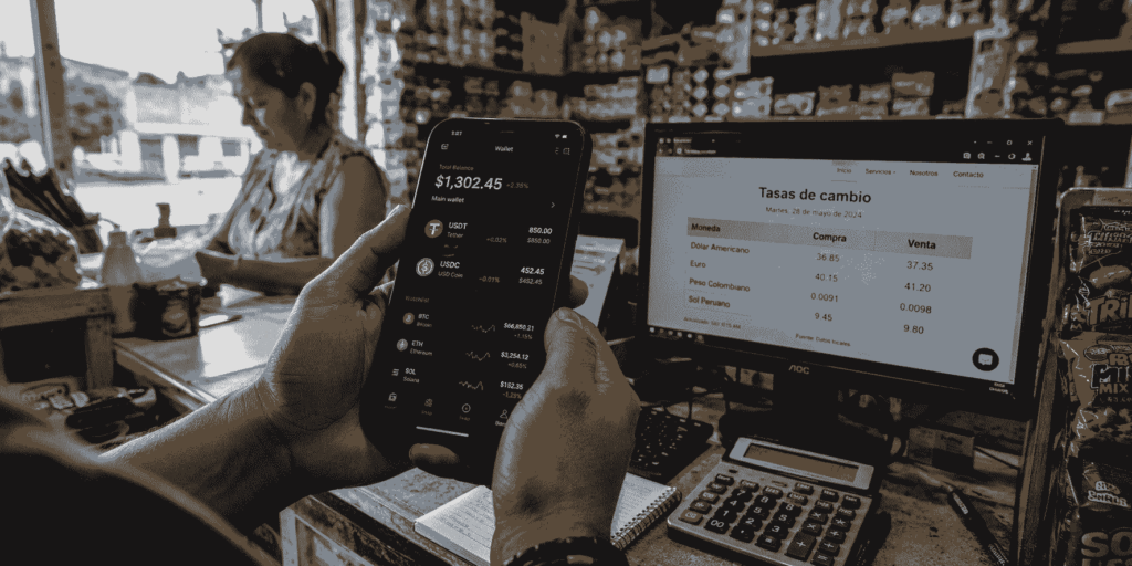 Fotografía documental en formato panorámico de primer plano de las manos de una persona sosteniendo un teléfono inteligente dentro de un pequeño comercio latinoamericano. En la pantalla del celular se observa una aplicación de billetera digital con saldos en USDT y USDC junto a gráficos financieros. Al fondo, de forma desenfocada, se aprecian estantes con productos cotidianos y un monitor de computadora con tasas de cambio de divisas locales.