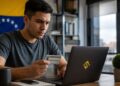 Hombre en Venezuela verificando su identidad con documento en mano frente a laptop.