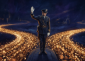Wide cinematic shot, 16:9. A lone traffic-police figure in an old-fashioned uniform stands in the middle of a vast flowing river of golden light, arm raised in a "halt" gesture. The luminous current of countless small particles streams past him on both sides, completely indifferent, never touching him. He is solid but powerless; the flow is unstoppable. Dark background, deep blues and blacks, the river glowing amber-gold like Bitcoin. Solemn, slightly melancholic mood. Photorealistic with a painterly quality. No text.