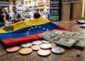 Dólares en efectivo junto a monedas de USDT sobre una mesa con la bandera de Venezuela.