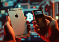 Una persona sosteniendo un telefono iphone y una hardware wallet para almacenar criptomonedas.