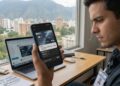 Hombre joven revisando en su smartphone la tarjeta virtual OKX Visa Platinum en Venezuela, sentado en un escritorio con laptop, fondo panorámico de Caracas con montañas, estilo realista y profesional.
