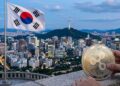 Una moneda metálica de Ripple USD (RLUSD) en primer plano con el horizonte urbano de Seúl y la bandera de Corea del Sur de fondo.