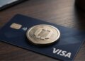 Tarjeta Visa con una moneda física dorada encima.