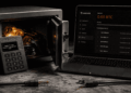 Fotografía conceptual en tono oscuro que muestra una billetera física Coldcard MK4 apoyada sobre una caja fuerte de metal abierta llena de monedas de Bitcoin. A la derecha, la pantalla de una computadora portátil en modo oscuro muestra la aplicación Wasabi Wallet con un balance en cero y varias salidas de fondos recientes. En primer plano hay un cable de red cortado sobre la superficie de piedra.