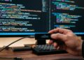 Una wallet de Ledger con un monitor al fondo que muestra lenguaje de programación