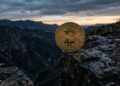 Moneda de Bitcoin al borde de un precipicio al atardecer.