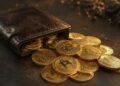 Cartera de cuero abierta derramando monedas doradas de bitcoin sobre una superficie oscura.