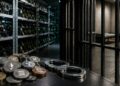 Monedas de criptomonedas y esposas en primer plano con una granja de minería y una celda de prisión al fondo.