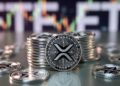 Monedas físicas de XRP y al fondo, desenfocado, aparece un gráfico de precios.