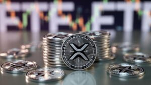 Monedas físicas de XRP y al fondo, desenfocado, aparece un gráfico de precios.
