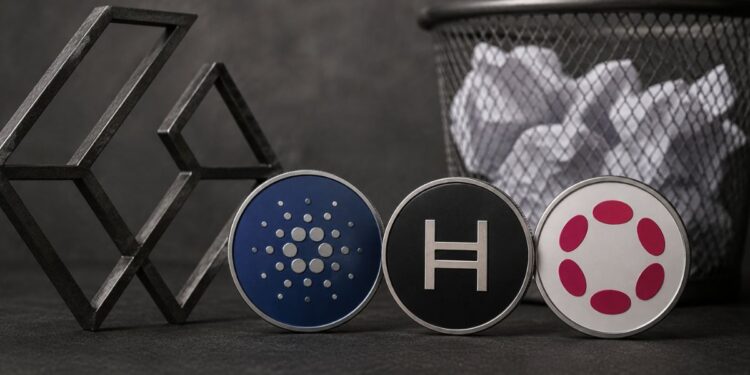 Monedas físicas con los logos de Cardano, Hedera y Polkadot junto a una papelera de reciclaje.