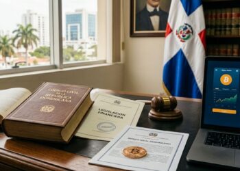 Una moneda física de Bitcoin sobre un documento oficial junto a leyes financieras en un escritorio, con la bandera dominicana de fondo.