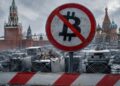 Señal de prohibición de Bitcoin frente al Kremlin en Moscú, rodeada de equipos de minería de criptomonedas dañados.