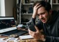 Un hombre con cara de desespero, con una Coldcard en la mano y monedas de bitcoin alrededor.