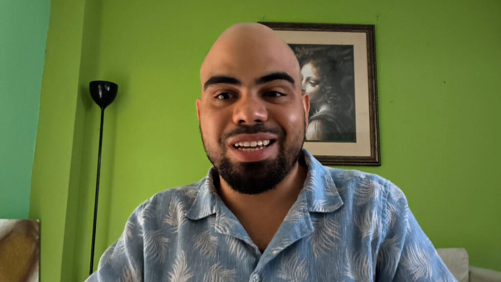 Forte 11, fundador de Cuba Bitcoin y el entrevistado del podcast Separando el dinero del Estado de criptoNoticias. Forte11 está sonriendo con camisa azul estampada sobre un fondo de pared verde.