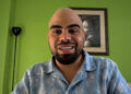 Forte 11, fundador de Cuba Bitcoin y el entrevistado del podcast Separando el dinero del Estado de criptoNoticias. Forte11 está sonriendo con camisa azul estampada sobre un fondo de pared verde.