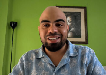 Forte 11, fundador de Cuba Bitcoin y el entrevistado del podcast Separando el dinero del Estado de criptoNoticias. Forte11 está sonriendo con camisa azul estampada sobre un fondo de pared verde.