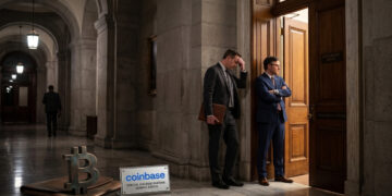 Un grupo de funcionarios vestidos con trajes formales se encuentra en el pasillo iluminado de un edificio gubernamental, mostrando expresiones de frustración y tensión junto a la puerta abierta de una sala de conferencias. En el suelo del corredor destacan una escultura de bronce con el símbolo de Bitcoin y un letrero con el logotipo de Coinbase.