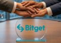 Personas en traje estrechando y uniendo sus manos sobre una placa transparente con el logo de Bitget en una mesa de reuniones.