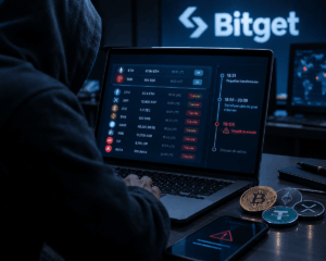 Persona encapuchada frente a una laptop con transacciones de criptomonedas y una alerta de seguridad, en una escena que representa el hackeo de Bitget.