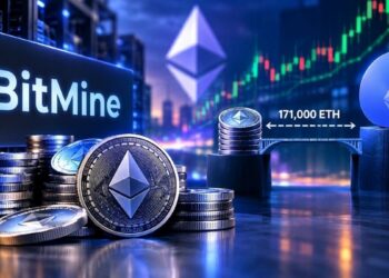 Una pila de criptomonedas Ethereum en primer plano con un gran monitor en el fondo que muestra el logotipo de BitMine.