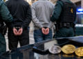 Dos personas esposadas custodiadas por la Guardia Civil junto a monedas físicas de criptomonedas Ethereum, Solana y XRP.