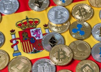 Muchas criptomonedas y detrás la bandera de España.
