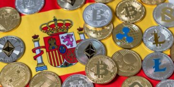 Muchas criptomonedas y detrás la bandera de España.